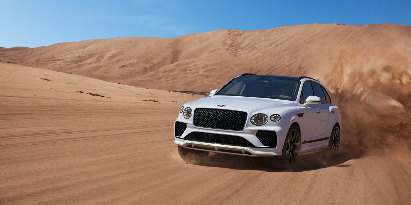 Bentley Dubai Bentley Bentayga Speed SUV front three quarter in Snow Quarts Pearlescent by Mulliner white paint driving dynamically through the desert