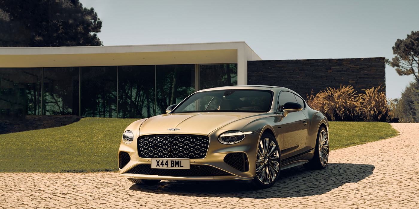 Bentley Dubai Bentley Continental GT Mulliner coupe front three quarters in Patina paint parked outside a glass fronted building with a grass lawn behind it