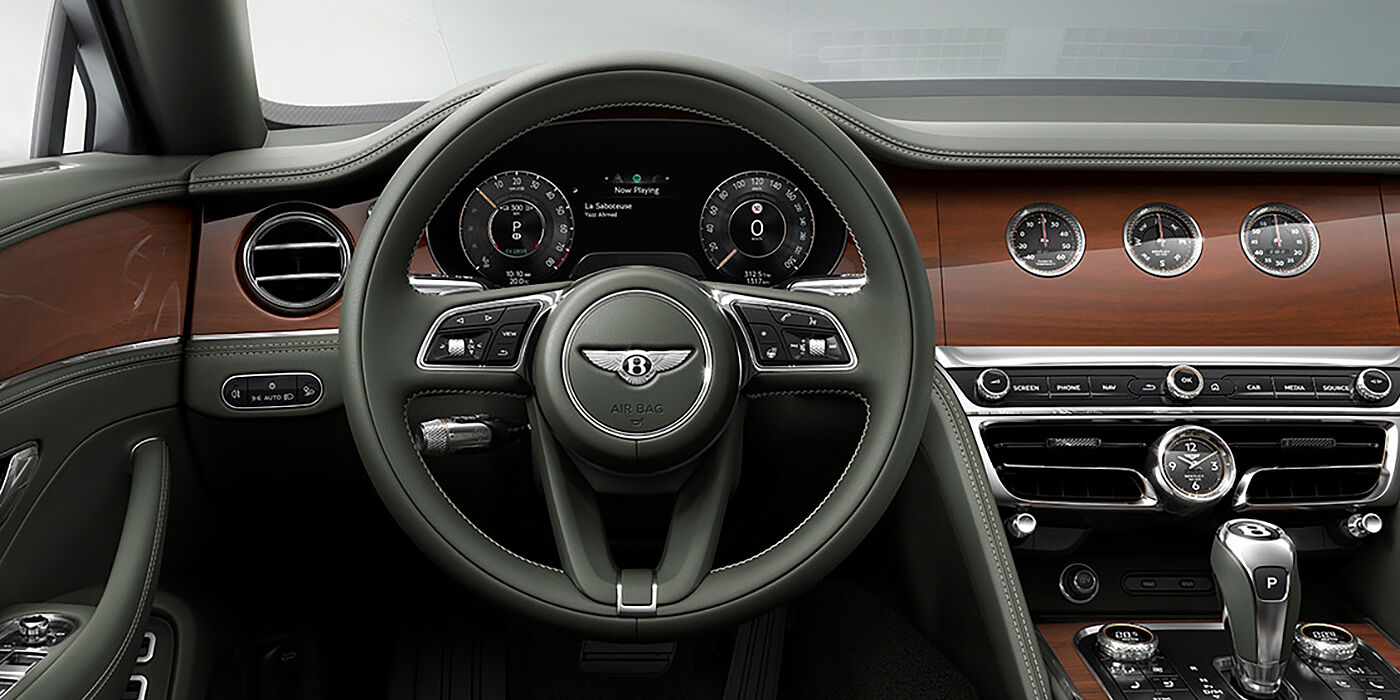 Bentley Dubai New Bentley Flying Spur sedan front cabin in Cumbrian Green hide and Crown Cut walnut veneer showing steering wheel and Rotating Display with three clocks on face