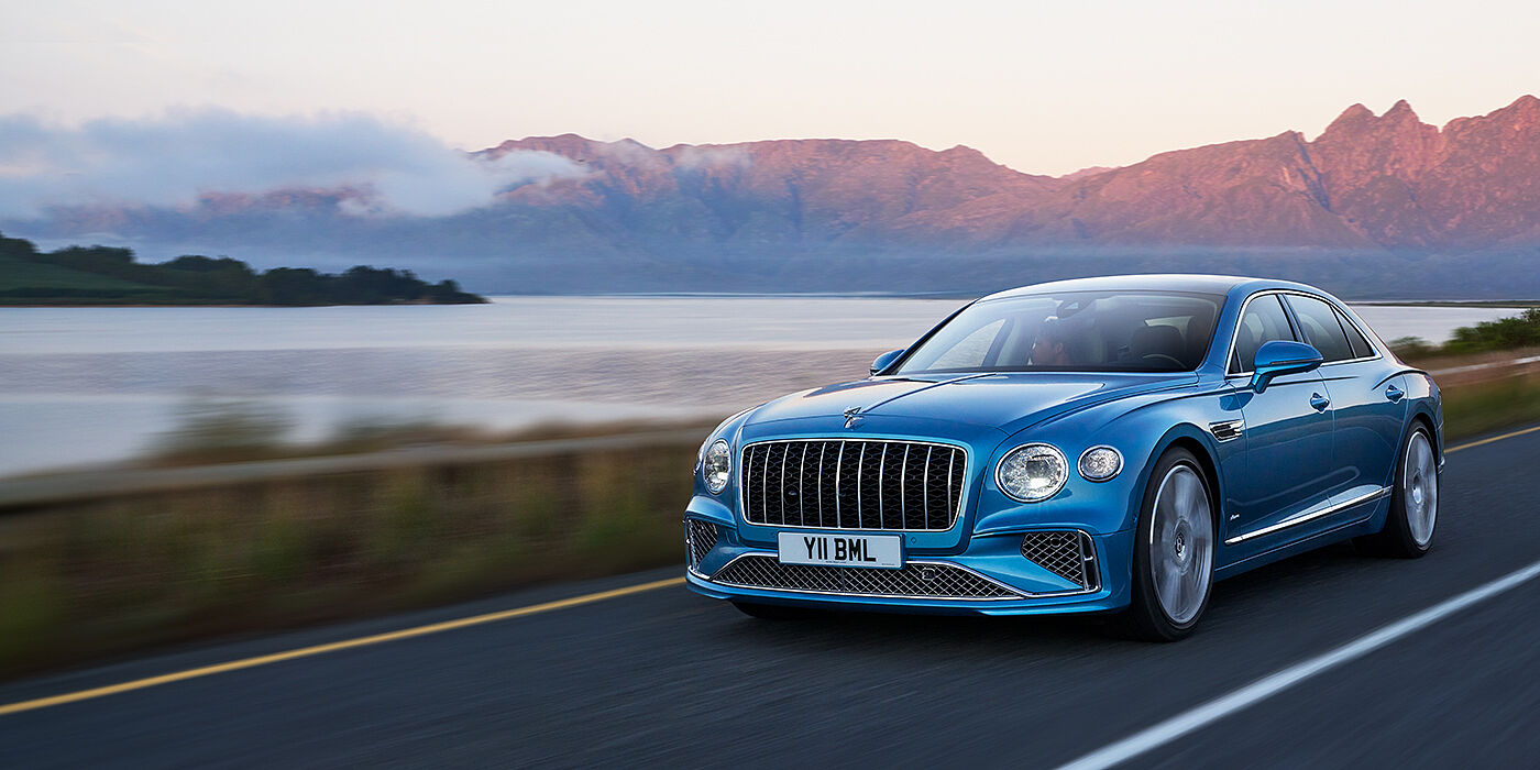 Bentley Dubai New Bentley Flying Spur Azure sedan in Light windsor blue paint by Mulliner, with 22 inch Azure wheels and chrome straight vaned grille driving on a mountain road