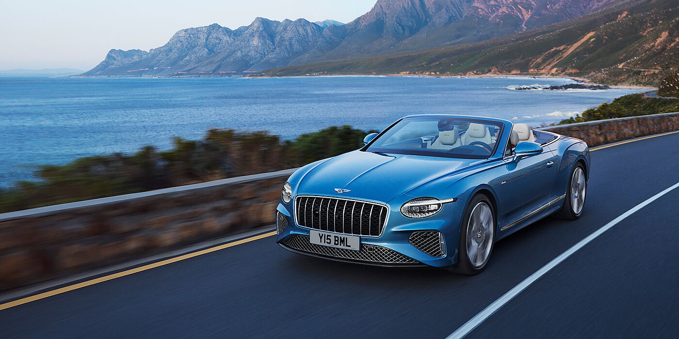 Bentley Dubai New Bentley Continental GTC Azure convertible in Light Windsor blue paint with 22 inch Azure wheels and chrome grill, driving dynamically by the sea