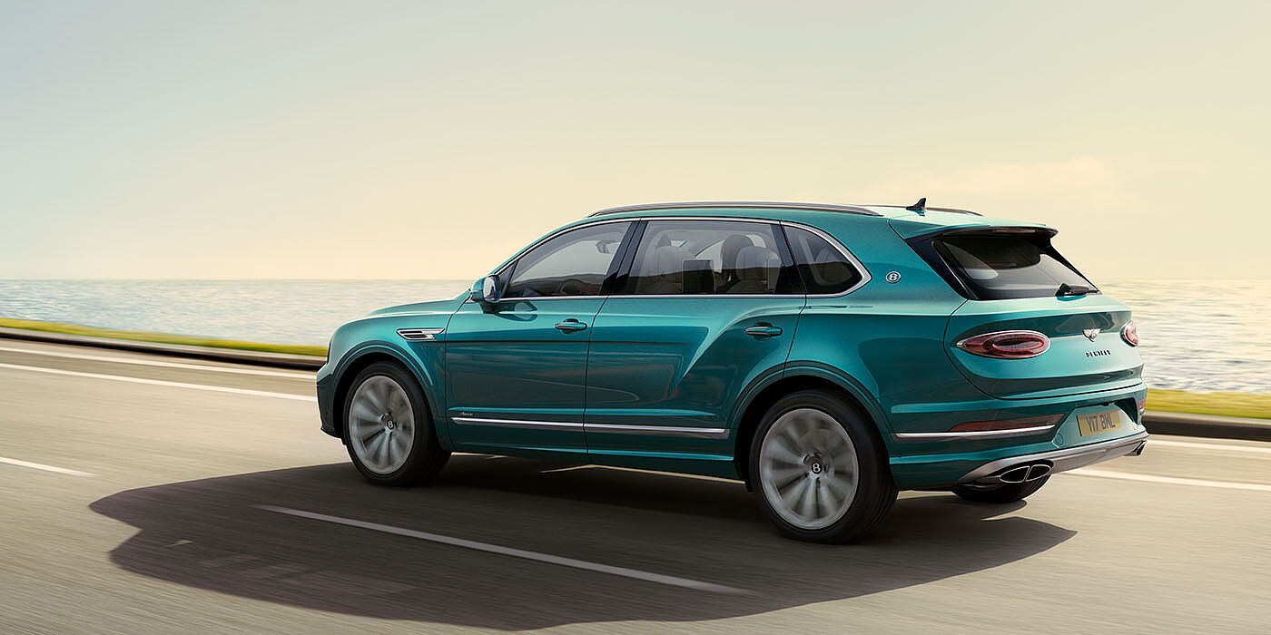 Bentley Dubai Bentley Bentayga Extended Wheelbase Azure luxury SUV rear three quarter in Topaz Blue by Mulliner paint, driving on an ocean road.