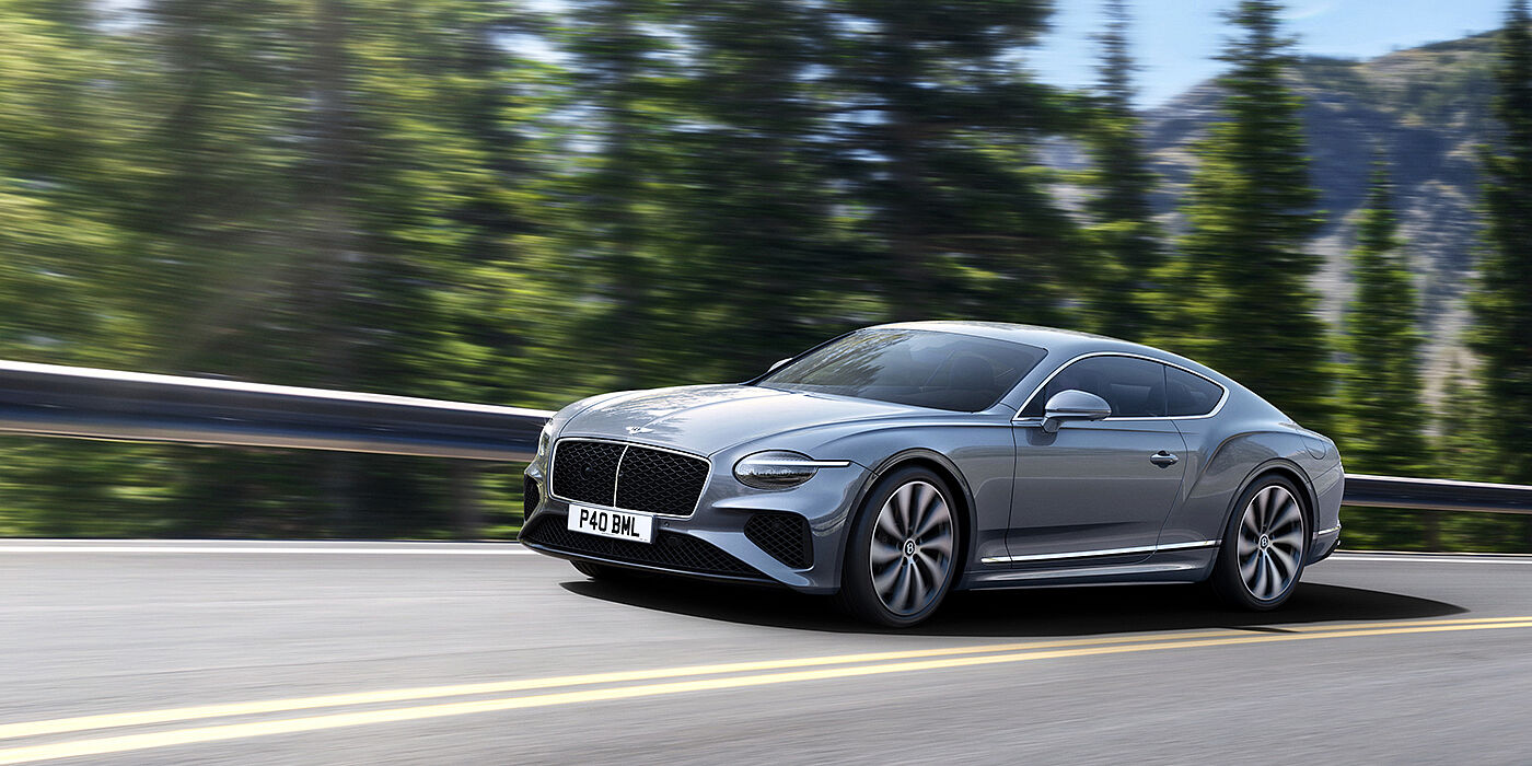 Bentley Dubai New Bentley Continental GT coupe in Silverlake paint and 22 inch ten-spoke wheels, driving dynamically on a tree-lined road in the sunshine