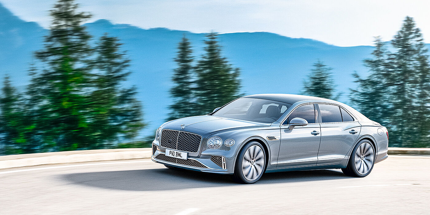 Bentley Dubai New Bentley Flying Spur sedan side view in Silverlake paint with ten spoke wheels and chrome matrix grille driving dynamically on a mountain road