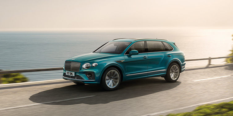 Bentley Dubai Bentley Bentayga Extended Wheelbase Azure SUV in Topaz blue paint driving dynamically by the ocean