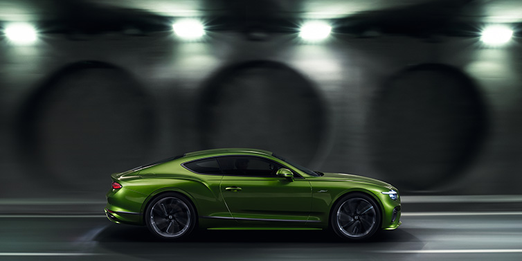 Bentley Dubai Bentley Continental GT Speed coupe profile in Tourmaline Green driving dynamically past a concrete wall at night