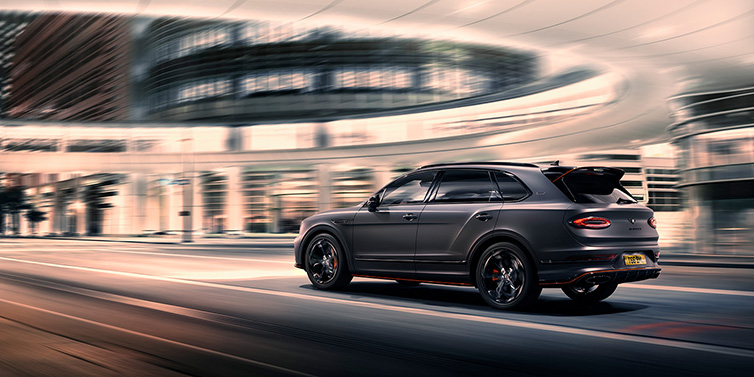 Bentley Dubai Bentley Bentayga S Black Edition SUV rear three quarter in Anthracite Satin paint driving dynamically through a city at night