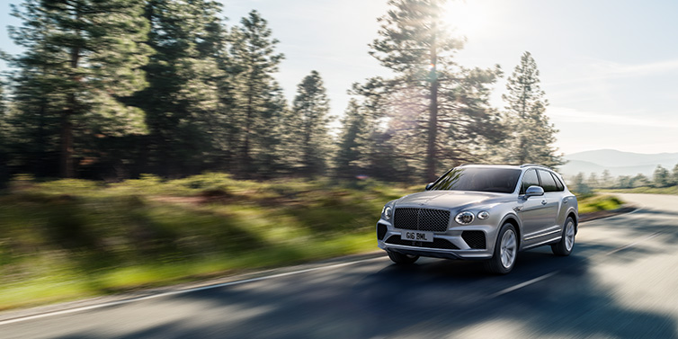 Bentley Dubai Bentley Bentayga SUV front three quarter in Moonbeam silver paint driving dynamically along a tree-lined road