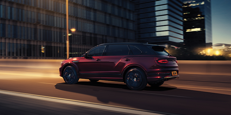 Bentley Dubai Bentley Bentayga Extended Wheelbase Mulliner SUV in Cricket Ball red paint driving dynamically in city at night