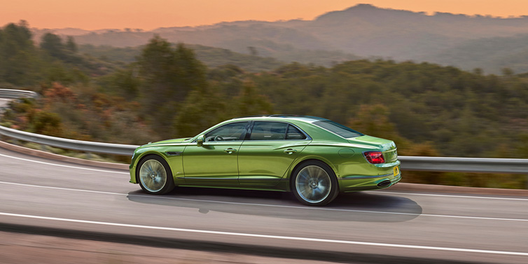 Bentley Dubai Bentley Flying Spur Speed sedan side profile in Tourmaline Green paint driving dynamically on a mountain road at sunset