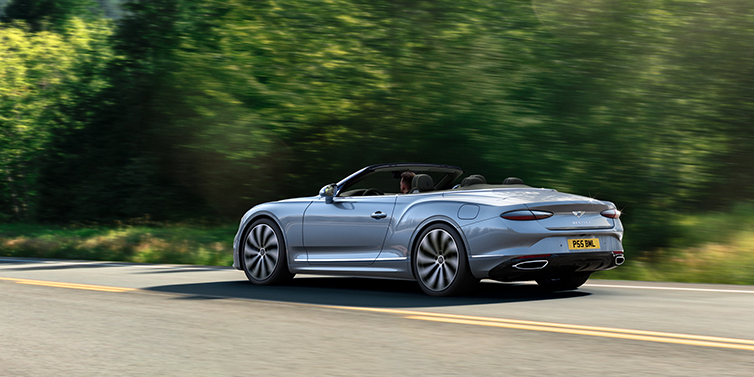 Bentley Dubai New Bentley Continental GTC convertible side view in Silverlake paint with 22 inch ten spoke wheels driving dynamically on a country road