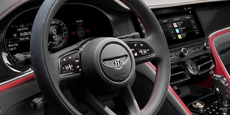 Bentley Dubai Bentley Flying Spur Speed sedan front interior detail showing steering wheel and driver screens surrounded with Hotspur red and Gravity Grey hides